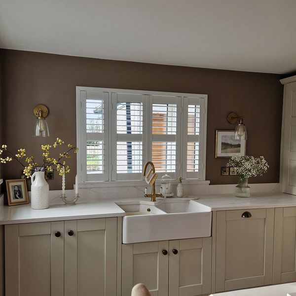 White plantation shutters above a belfast sink in a warm kitchen