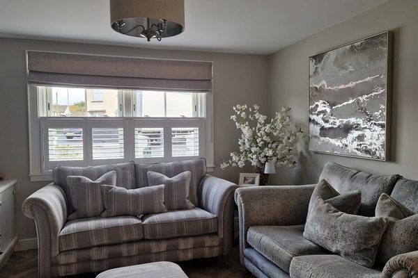 Living room with a roman blind and shutters at the window and two grey sofas