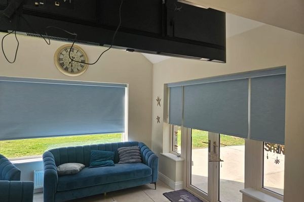 Teal roller blinds fitted across a sunroom window and patio doors
