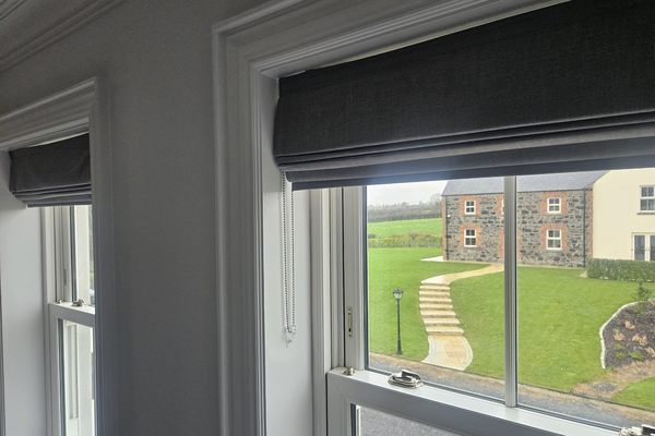 Charcoal roman blinds fitted above sash windows looking out over a lawn to a stone building