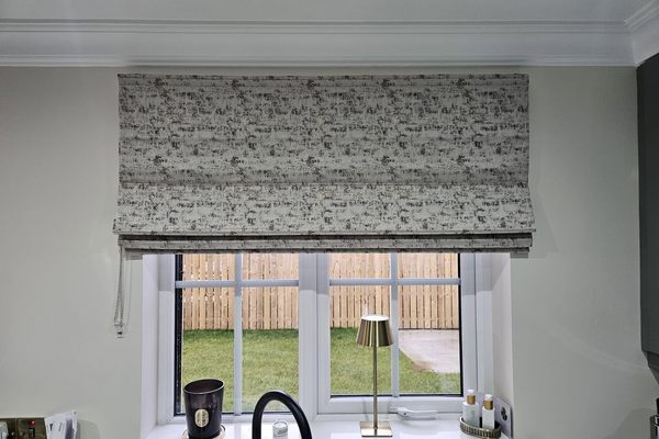 Textured grey roman blind fitted above a kitchen window looking onto a garden